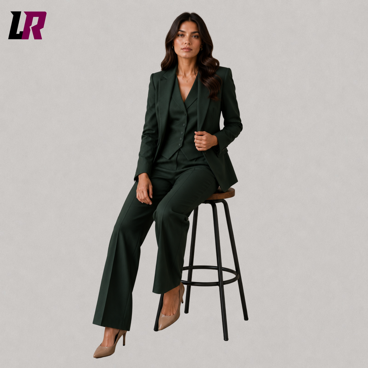Woman wearing a forest green formal suit set seated on a stool in a professional portrait