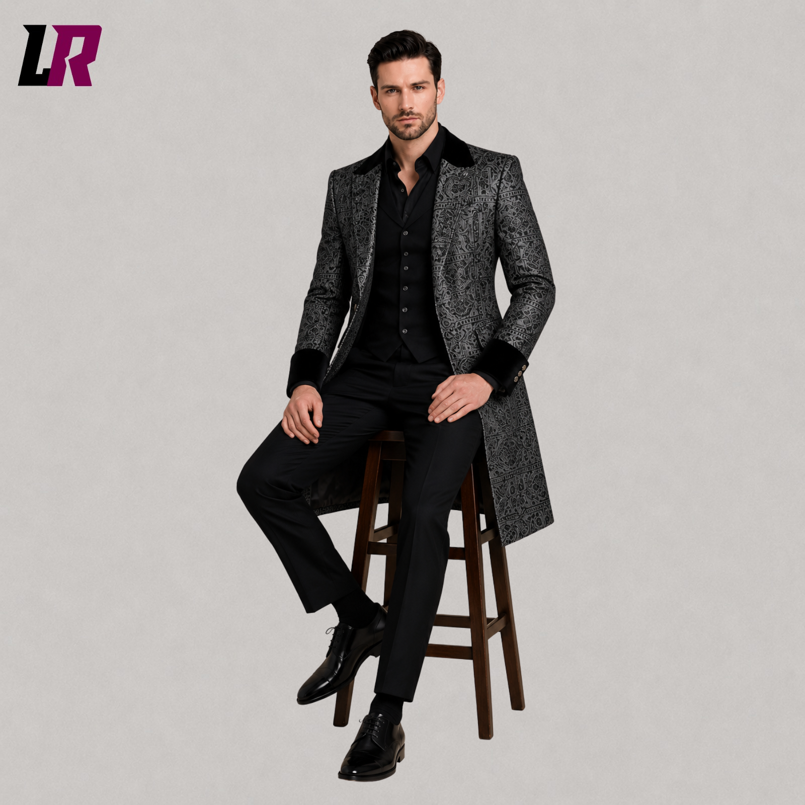 Men's black silver Victorian Gothic long coat with model seated on a stool in a luxury formal fashion pose