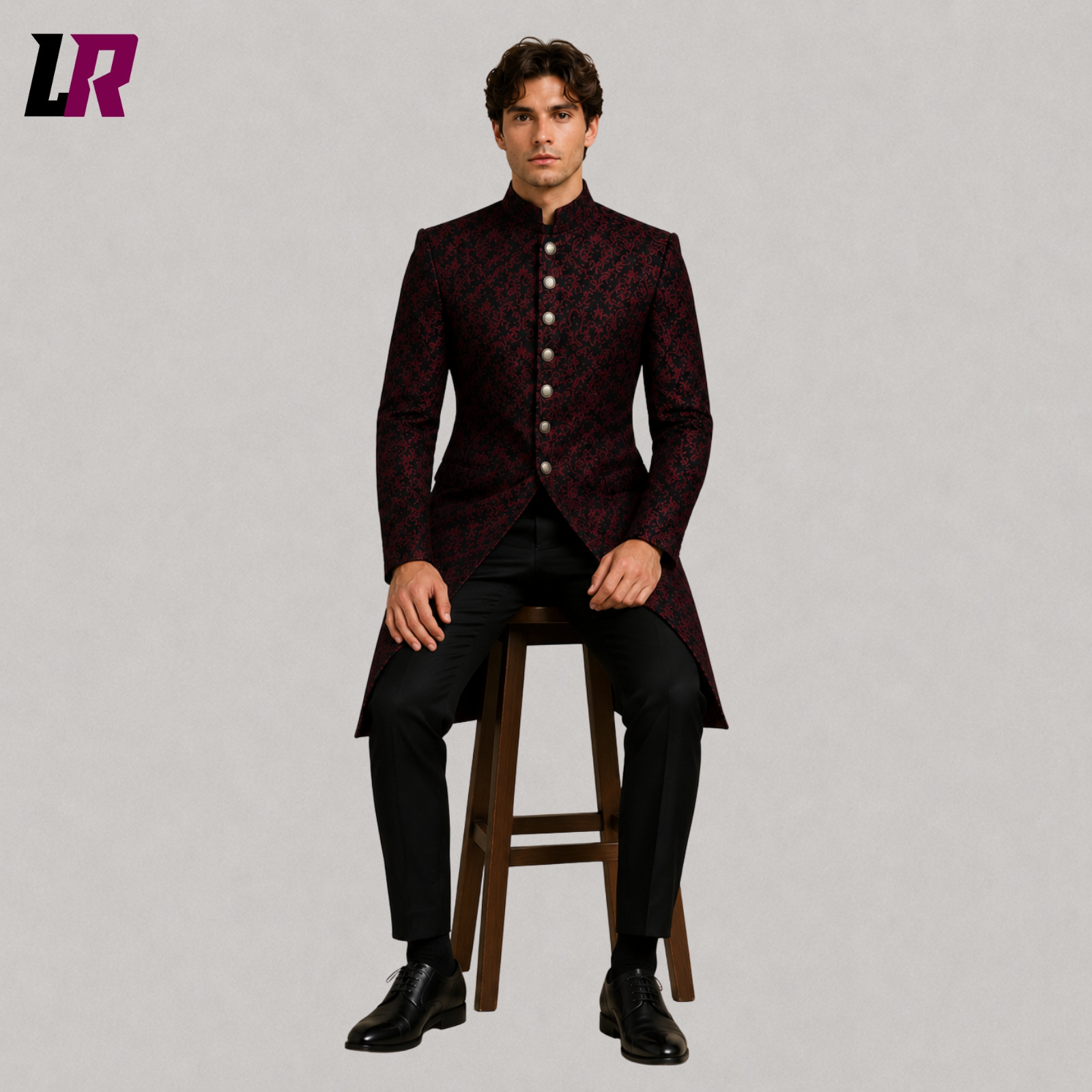 Men's red black brocade long coat with model seated on a stool in a luxury formal fashion pose