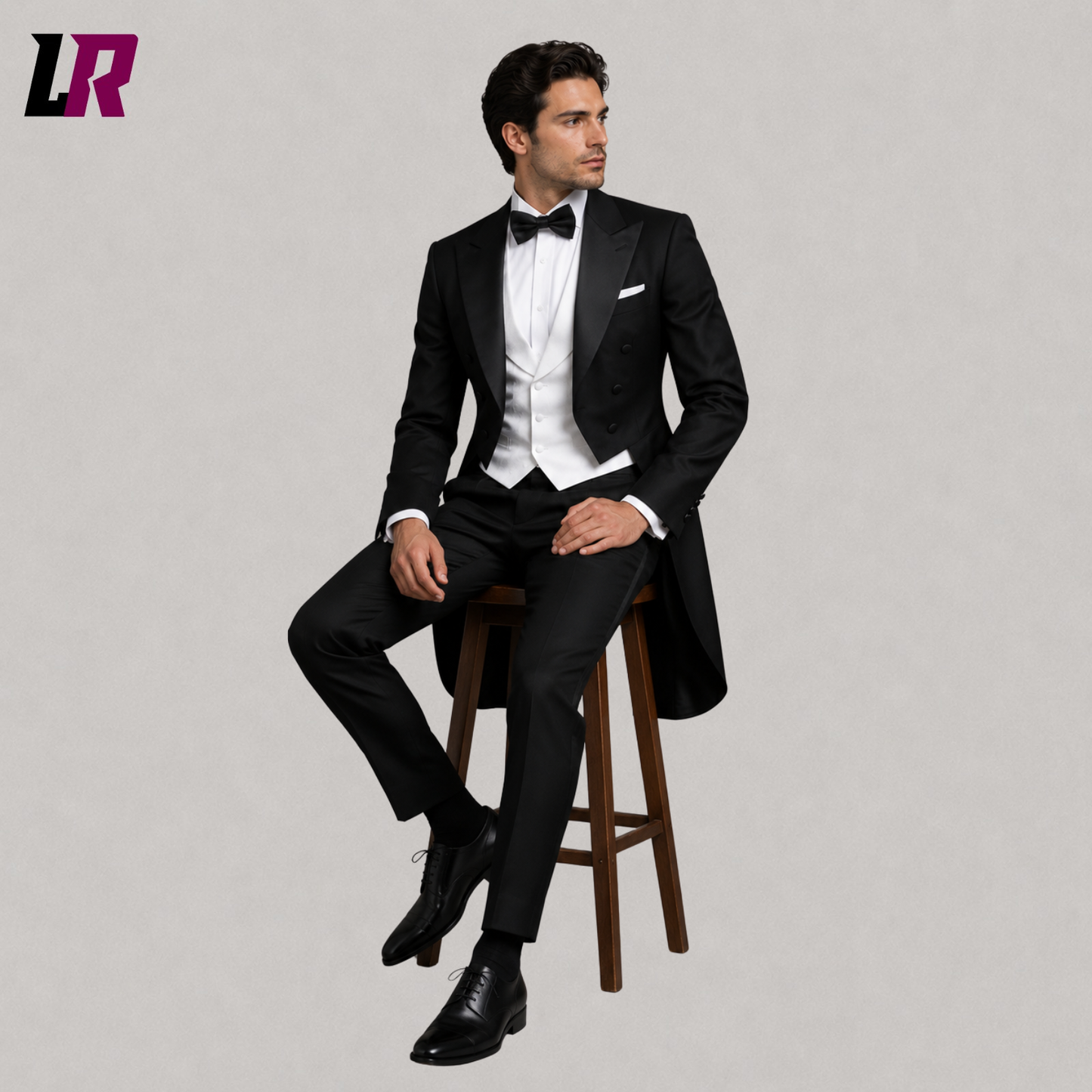 Man sitting on a stool wearing a black tailcoat tuxedo suit with white waistcoat and bow tie for weddings and formal events