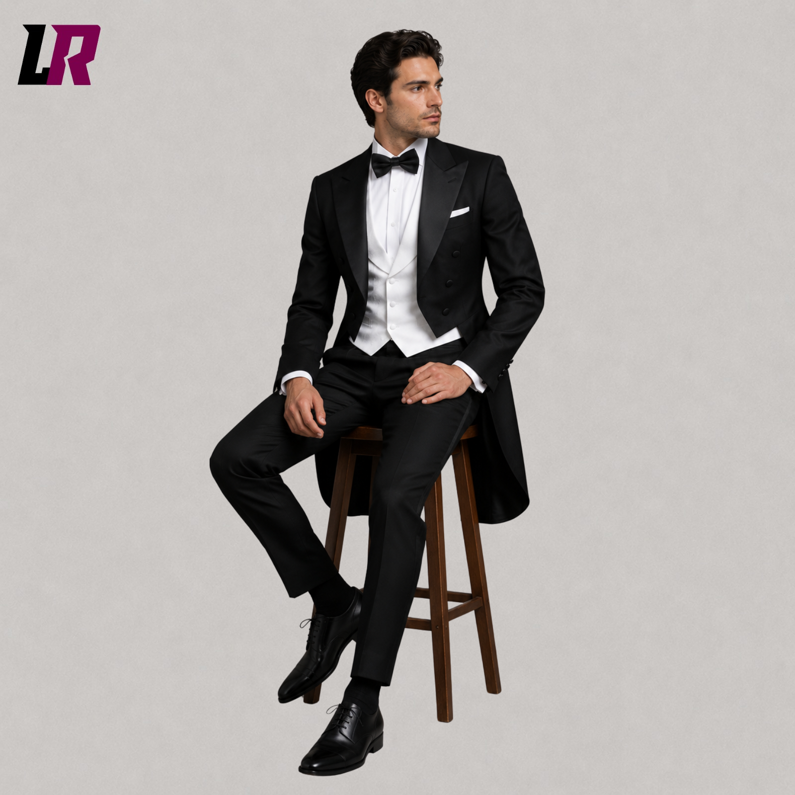 Man sitting on a stool wearing a black tailcoat tuxedo suit with white waistcoat and bow tie for weddings and formal events