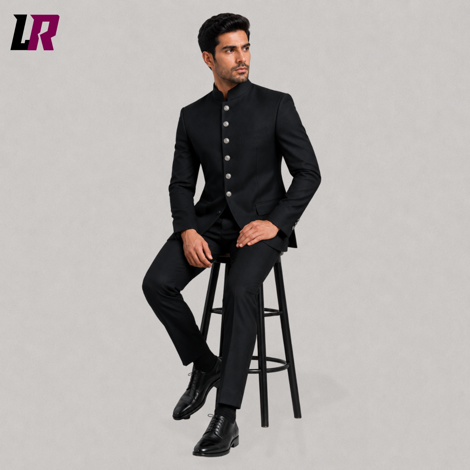 Man wearing a black Victorian Gothic Chinese Tunic Suit seated on a stool in a Regency Bandhgala jacket