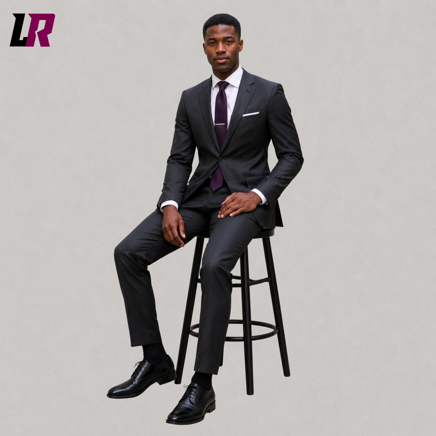 Man wearing a custom charcoal grey tailored suit seated on a stool in a formal portrait