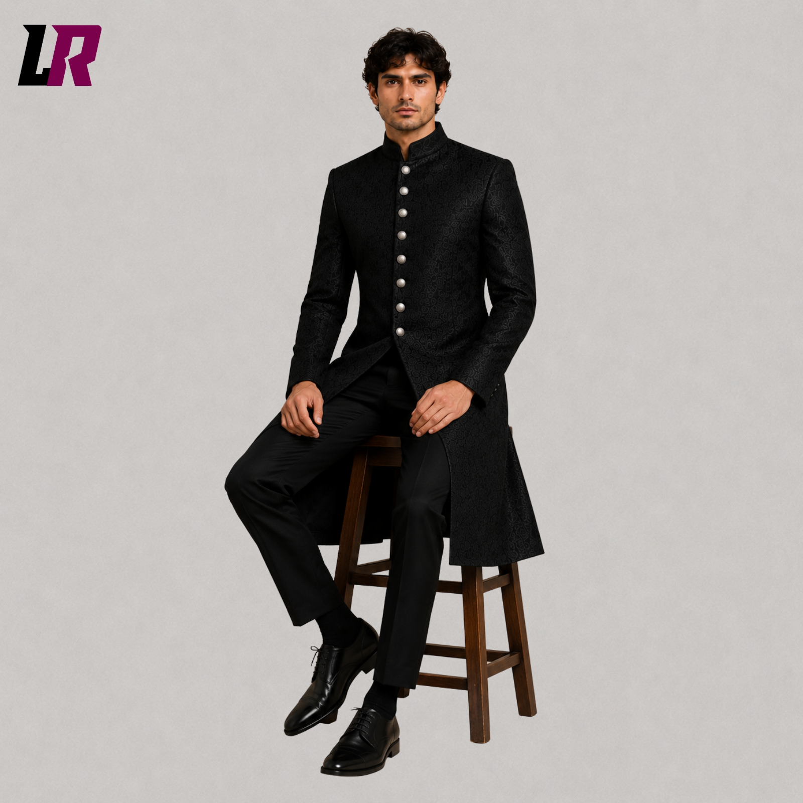 Men's black brocade sherwani coat with model seated on a stool in a luxury formal fashion pose