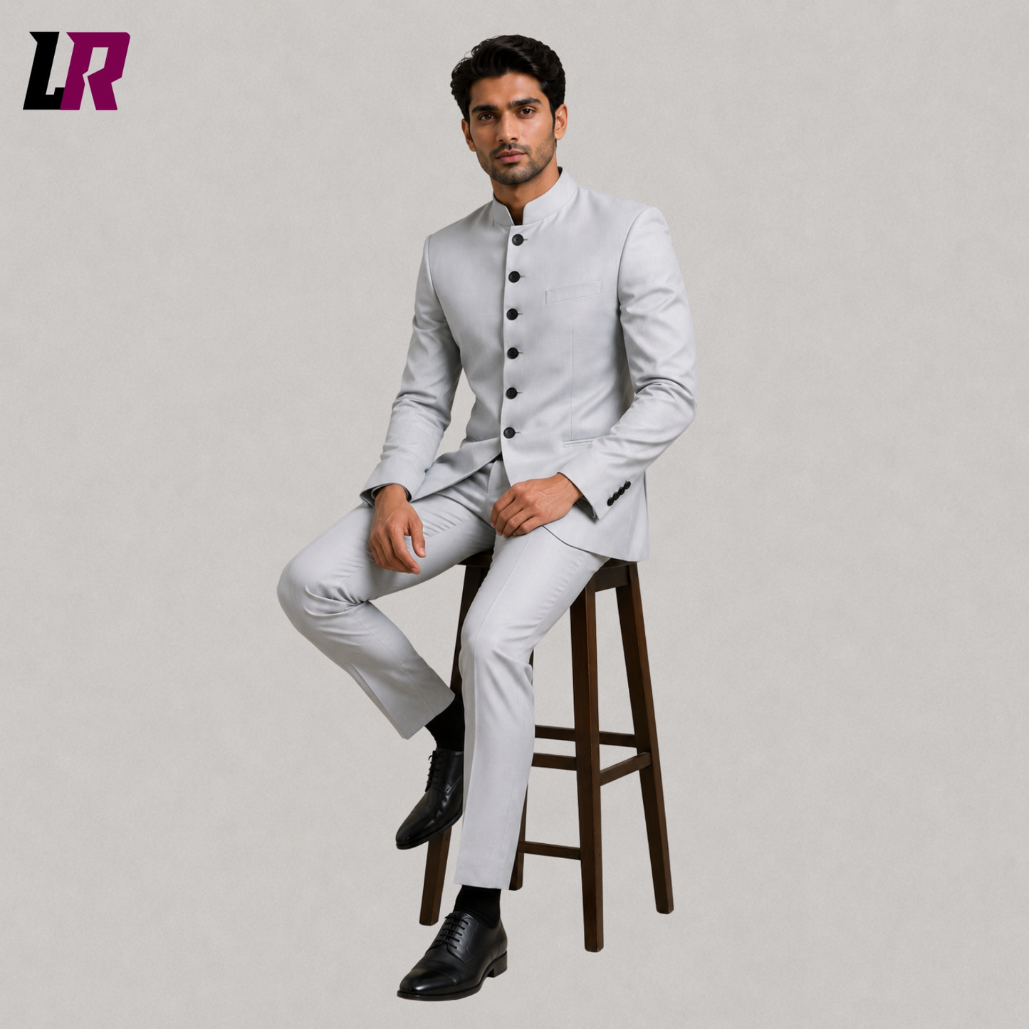 Man wearing a light grey Bandhgala suit with Mandarin collar seated on a stool in a formal portrait